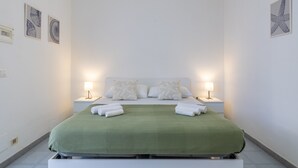 Una cama bien hecha con una colcha verde, dos almohadas blancas y dos lámparas de noche.