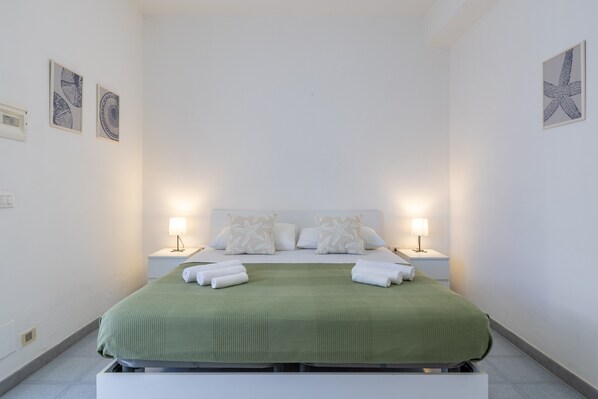 Un lit bien fait, avec une couvre-lit verte, deux oreillers blancs et deux lampes de chevet.