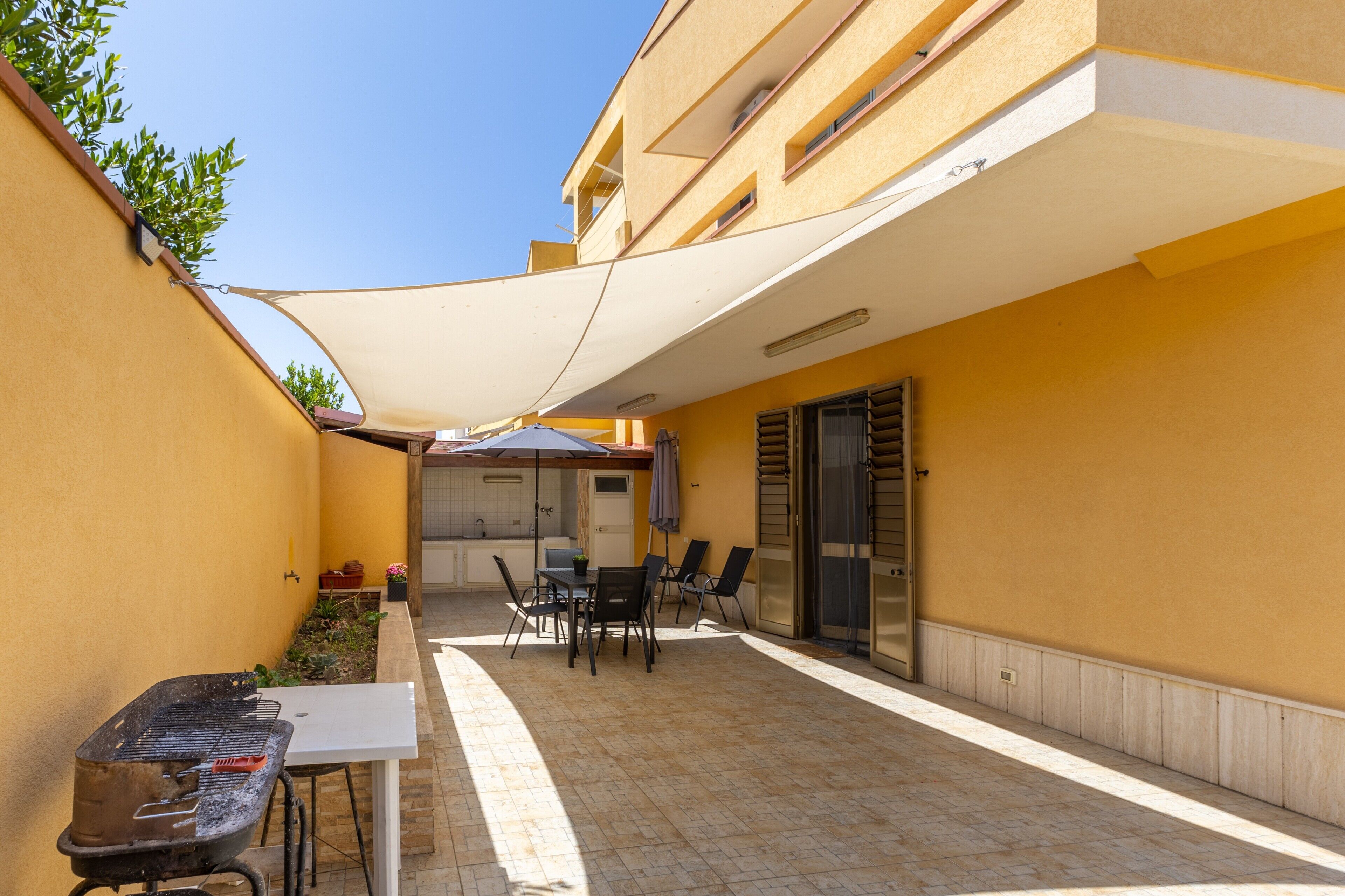 Un patio exterior con mesa y sillas, una parrilla y un área cubierta con mesa y sillas.
