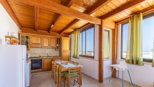 A kitchen with wooden cabinets, a dining table with chairs, a refrigerator, and a window with curtains. - Apartment 'Alta Marea' with Sea View, Wi-Fi and Air Conditioning (Ispica)