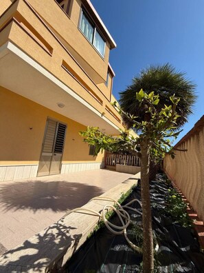 A building with a yellow facade, a door, and a small tree with green leaves.