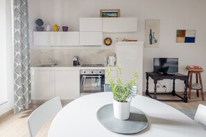 A modern kitchen with white cabinets, a coffee maker, a kettle, and a TV on a wooden table.