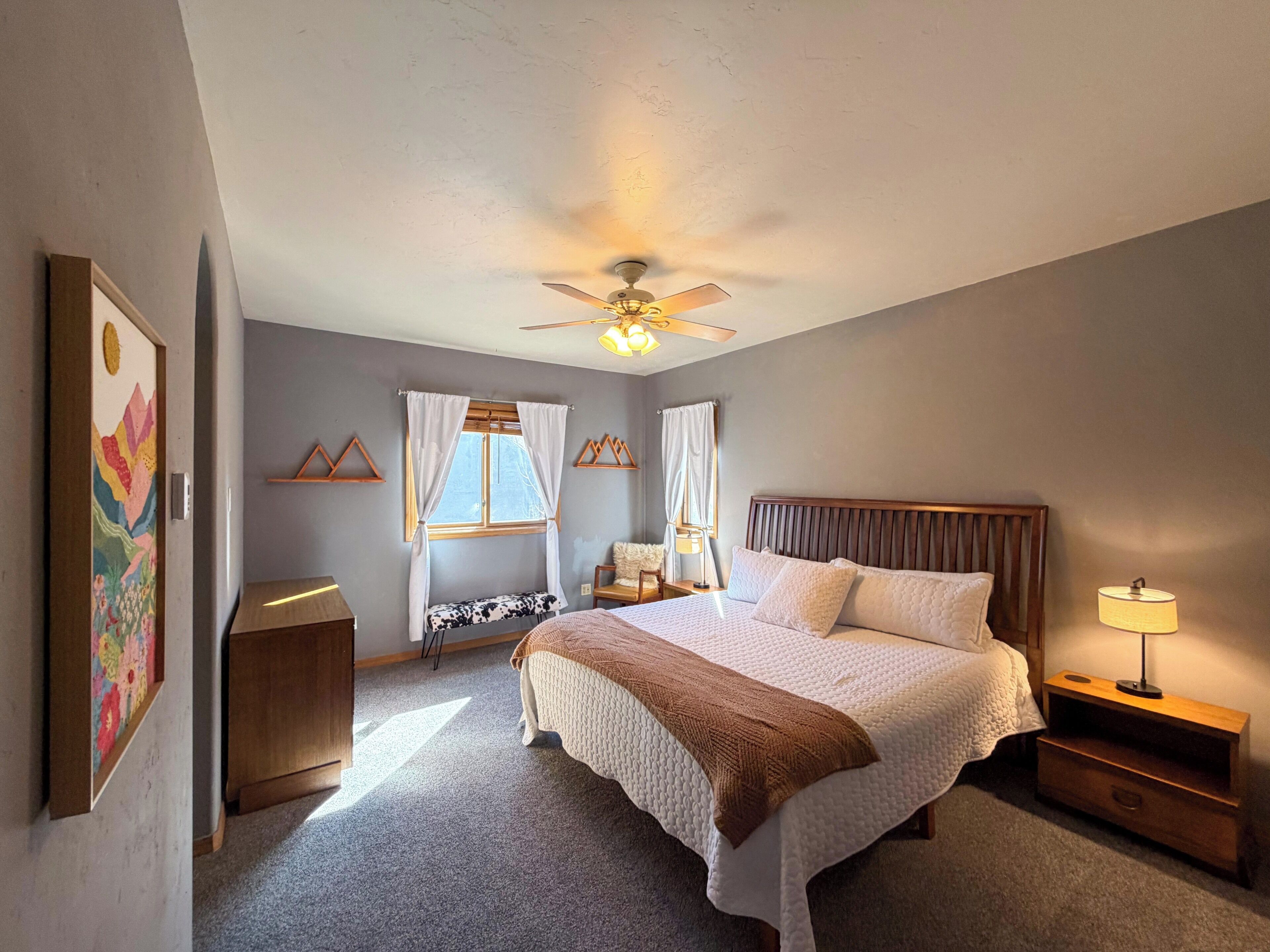 A bedroom with a bed, bedside tables, a ceiling fan, and a window with curtains.
