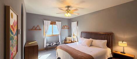 A bedroom with a bed, bedside tables, a ceiling fan, and a window with curtains.