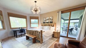 A bedroom with a large bed, a desk, a chair, a bench, and a view of an outdoor patio. - 4 BR-7 Bed-Durango Dream House-Incredible Mountain/Golf Views w/ Chef’s Kitchen (Durango)
