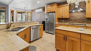 A modern kitchen with granite countertops, stainless steel appliances, wooden cabinets, and a brick backsplash. - 4 BR-7 Bed-Durango Dream House-Incredible Mountain/Golf Views w/ Chef’s Kitchen (Durango)