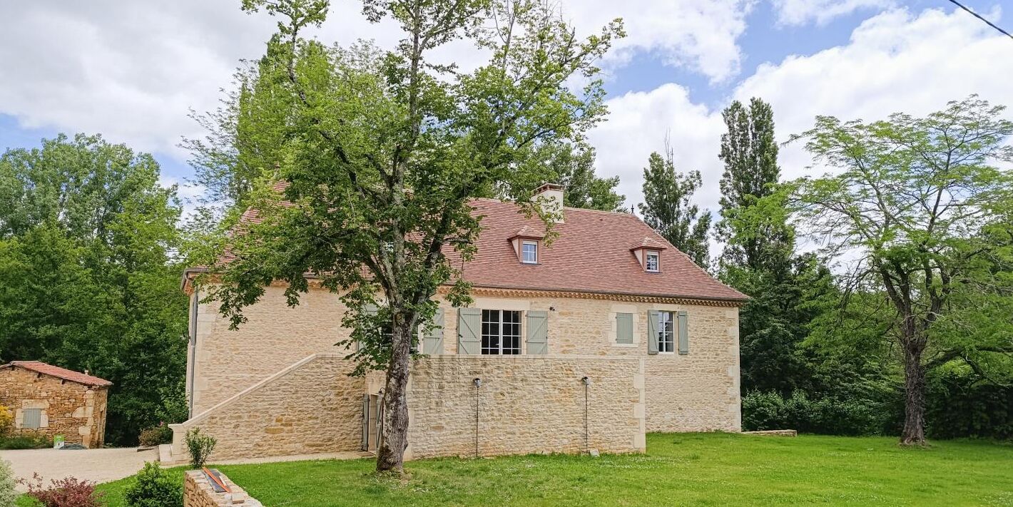 A stone building with a tiled roof, a grassy yard, and trees.