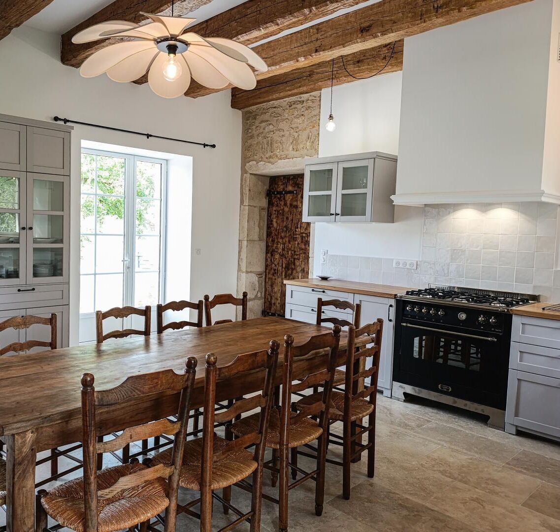 Una cocina con mesa y sillas de madera, estufa y armarios blancos.