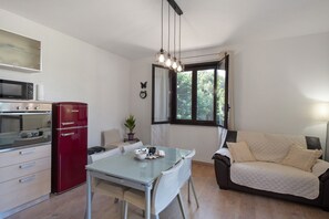 Un espacio habitable compacto con kitchenette, una mesa de comedor, un sofá y una ventana que ofrece vistas a la vegetación.