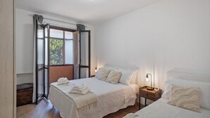 Camera da letto con due letti, pavimento in legno, finestra con tende e una lampada da comodino.