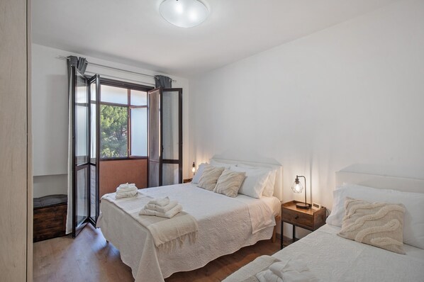 Un dormitorio con dos camas, suelo de madera, una ventana con cortinas y una lámpara de noche.
