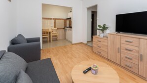 Een moderne woonkamer met een bank, een televisie, een houten kast en een keuken op de achtergrond.