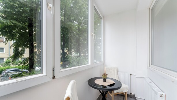Een hoekkamer met raam, een klein rond tafeltje met een plant, een witte stoel en een radiator.