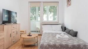 Een moderne hotelkamer met een bed, een televisie op een houten kast, een klein rond tafeltje en een raam met uitzicht op bomen en gebouwen.