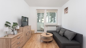 Een moderne woonkamer met een grijze bank, een houten kast, een ronde salontafel en een televisie op een meubel.