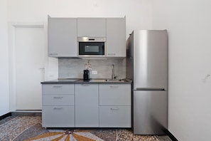 A modern kitchen with grey cabinets, a stainless steel refrigerator, and a microwave.