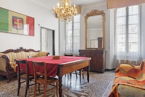 A dining area with a wooden table, chairs, a chandelier, a sofa, and a large mirror.