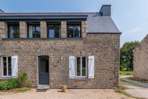 Ein Steinhaus mit dunklem Dach, einer Tür und zwei Fenstern mit weißen Fensterläden.