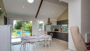 Une cuisine moderne dotée d’un grand  îlot central, d’un coin repas avec une table et des chaises, et offrant une vue sur l’extérieur.