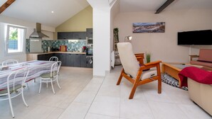 Une cuisine moderne avec un coin repas, un téléviseur à écran plat et un espace salon confortable comprenant un fauteuil et un canapé.