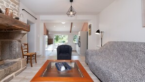 A modern living room with a stone fireplace, a glass-top coffee table, a leopard print sofa, and a view to the outside. - Charming House 'Au Pied Des Chênes' with Private Terrace, Shared Garden & Wi-Fi (Crach)