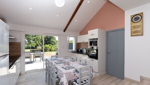 A modern kitchen with a dining area, wooden ceiling beams, and a clock on the wall. - Charming House 'Au Pied Des Chênes' with Private Terrace, Shared Garden & Wi-Fi (Crach)