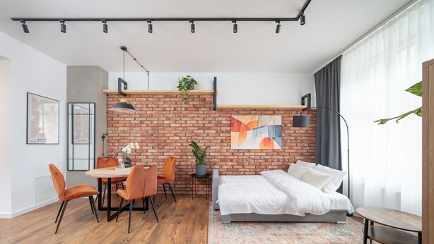 Un dormitorio moderno con pared de ladrillo, una cama, una mesa de comedor con sillas y una mesita de noche con una planta.