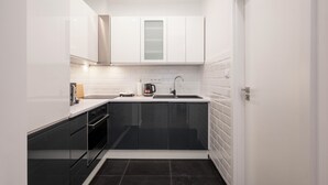 Cocina compacta con armarios blancos, encimera negra y salpicadero negro.