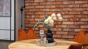Una mesa redonda de madera con un jarrón de flores y velas, frente a un muro de ladrillo.