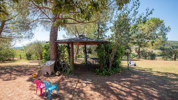 Un espace extérieur abrité, avec une table et des chaises, entouré d’arbres et offrant une vue sur un ciel dégagé.