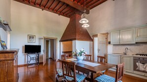 A dining area with a wooden table, chairs, a TV, and a kitchen with cabinets and appliances. - Apartment 'Memories' Farm Stay with View of Siena (Monteroni d'Arbia)