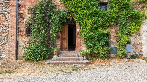 A rustic building with a wooden door, stone steps, and a gravel driveway. - Apartment 'Memories' Farm Stay with View of Siena (Monteroni d'Arbia)