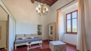 A room with a sofa, a table, a cabinet, and a window with curtains. - Apartment 'Memories' Farm Stay with View of Siena (Monteroni d'Arbia)