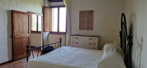 Une chambre à coucher avec un lit, une commode, un radiateur et une fenêtre avec des rideaux.