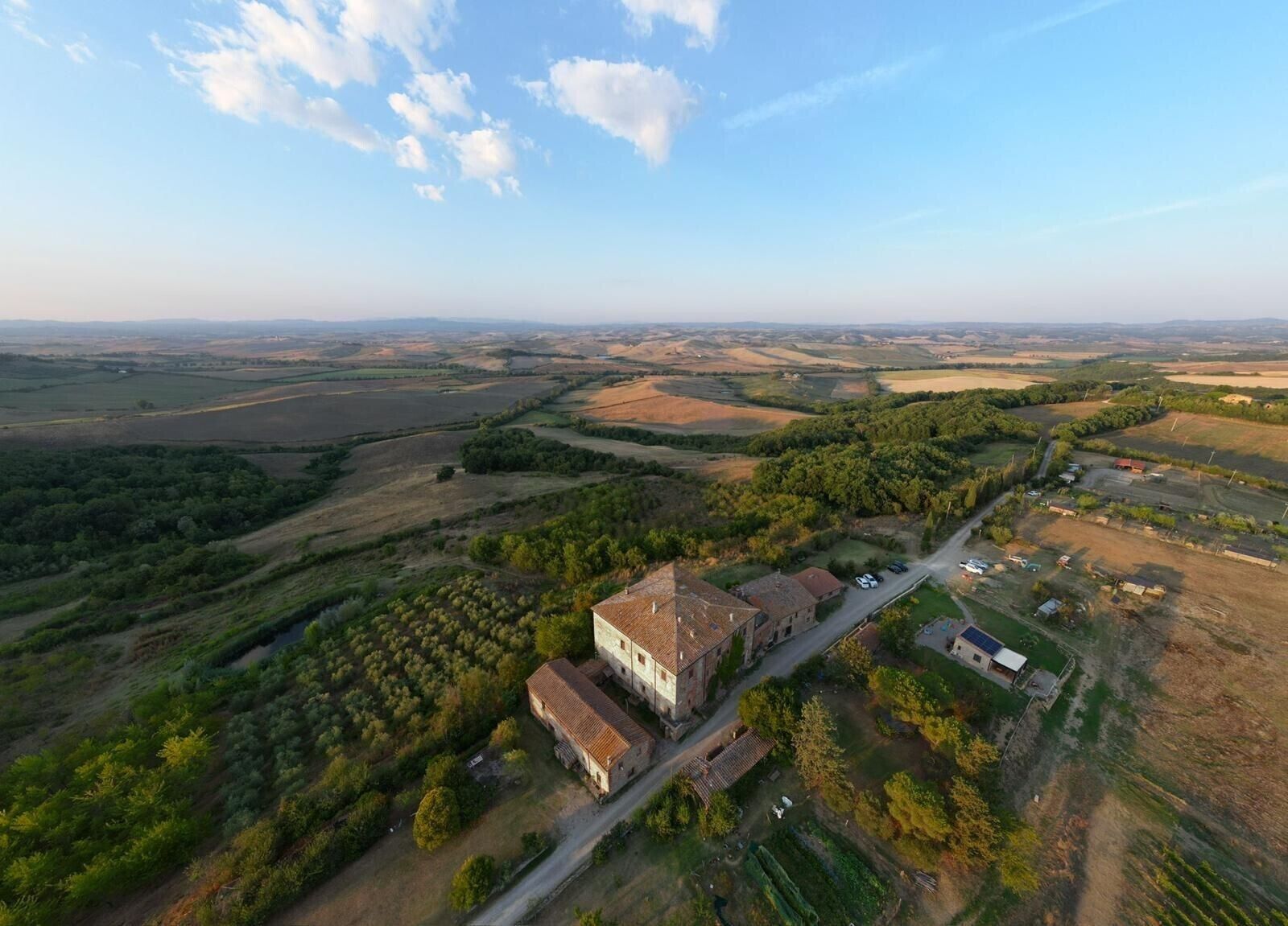An aerial view of a rural property with a large building, surrounded by fields and trees.