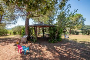 Un espace extérieur abrité, avec une table et des chaises, entouré d’arbres et offrant une vue sur un ciel dégagé.
