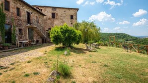 A rustic stone building with a staircase leading to a door, a small garden with a tree, and a bench. - Apartment 'Romantico' – Farm Stay with View of Siena (Monteroni d'Arbia)