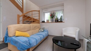 A living room with a sofa, a white chair, a glass table, and a TV. - Cottage 'Le Cocon' with Private Terrace, Shared Garden and Wi-Fi (Crach)