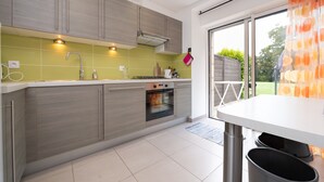 A modern kitchen with grey cabinets, a built-in oven, and a large window. - Cottage 'Le Cocon' with Private Terrace, Shared Garden and Wi-Fi (Crach)