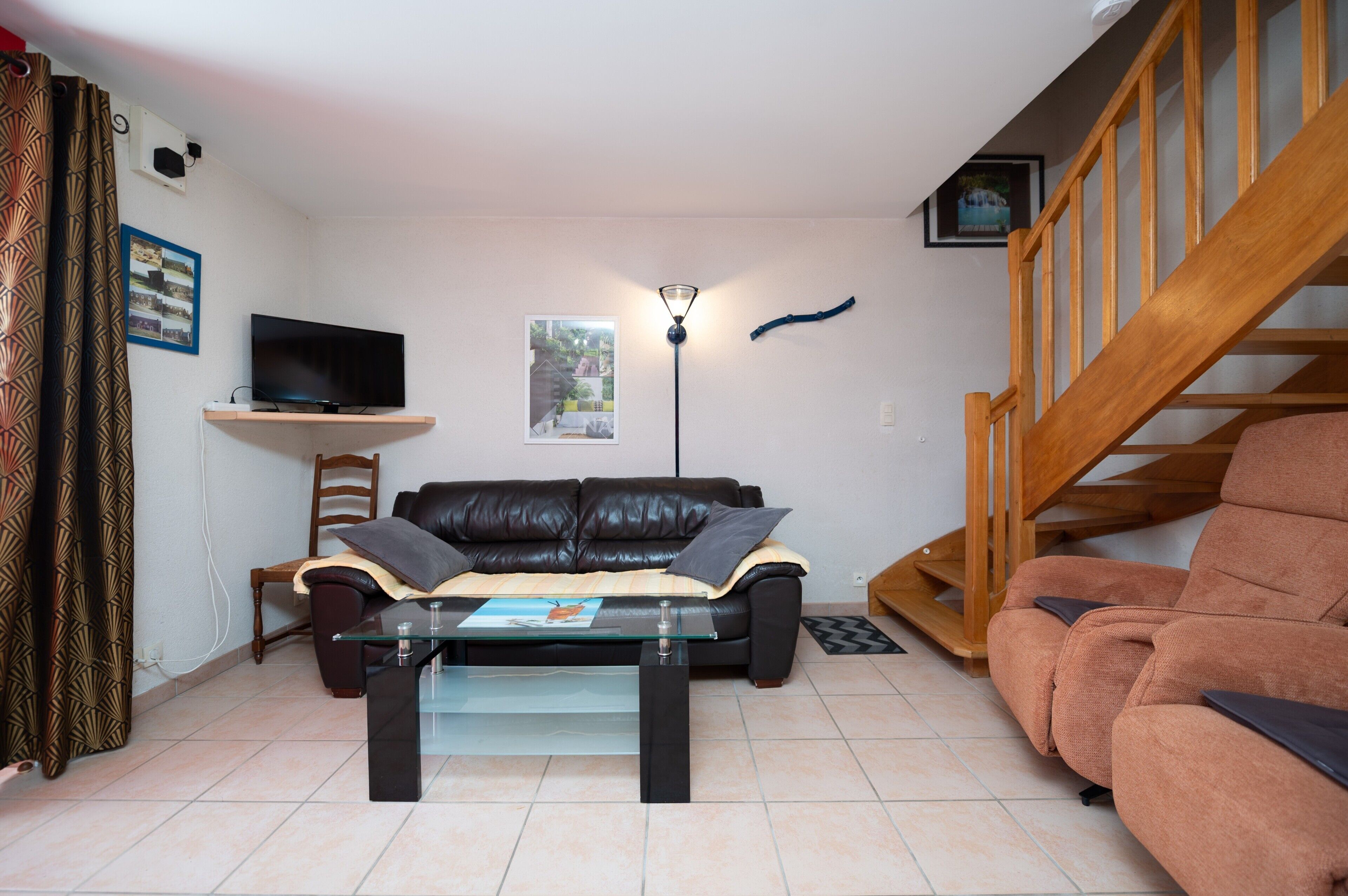 A living room with a sofa, a glass coffee table, a TV on a stand, a lamp, a chair, and a staircase.