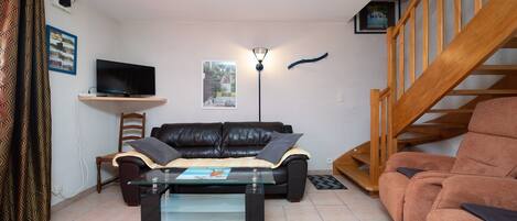 A living room with a sofa, a glass coffee table, a TV on a stand, a lamp, a chair, and a staircase.