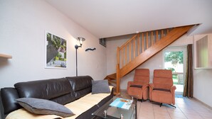 A living room with a sofa, two armchairs, a glass coffee table, a staircase, and a wall-mounted lamp.