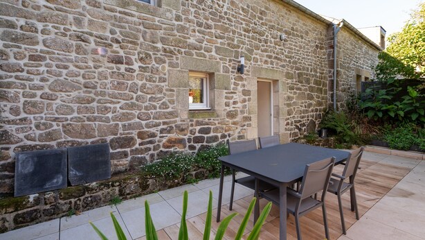 A stone building with a patio area, a table, and chairs.