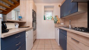 A compact kitchen with a built-in oven, microwave, and dishwasher, wooden cabinets, and a window providing natural light.