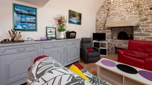Ein Wohnzimmer mit Kamin aus Stein, einer grauen Couch, einer roten Couch, einem Fernseher und einem Esstisch mit Blumen in einer Vase.