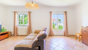 Ein Wohnzimmer mit einer Couch, einem Holzkasten, einem Fernseher und einem Fenster mit Vorhängen.