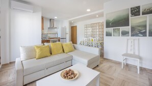 A modern living room with a white sofa, a coffee table, and a dining area with a patterned tablecloth.