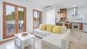 A modern living room with a sofa, a dining table, and a kitchen area with cabinets and appliances.