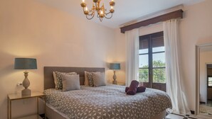 Quarto com piso xadrez, cama com roupa de cama estampada, duas luminárias de cabeceira, um lustre e janela com cortinas.