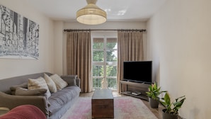 Uma sala de estar com sofá, mesa de centro, televisão e cortinas.